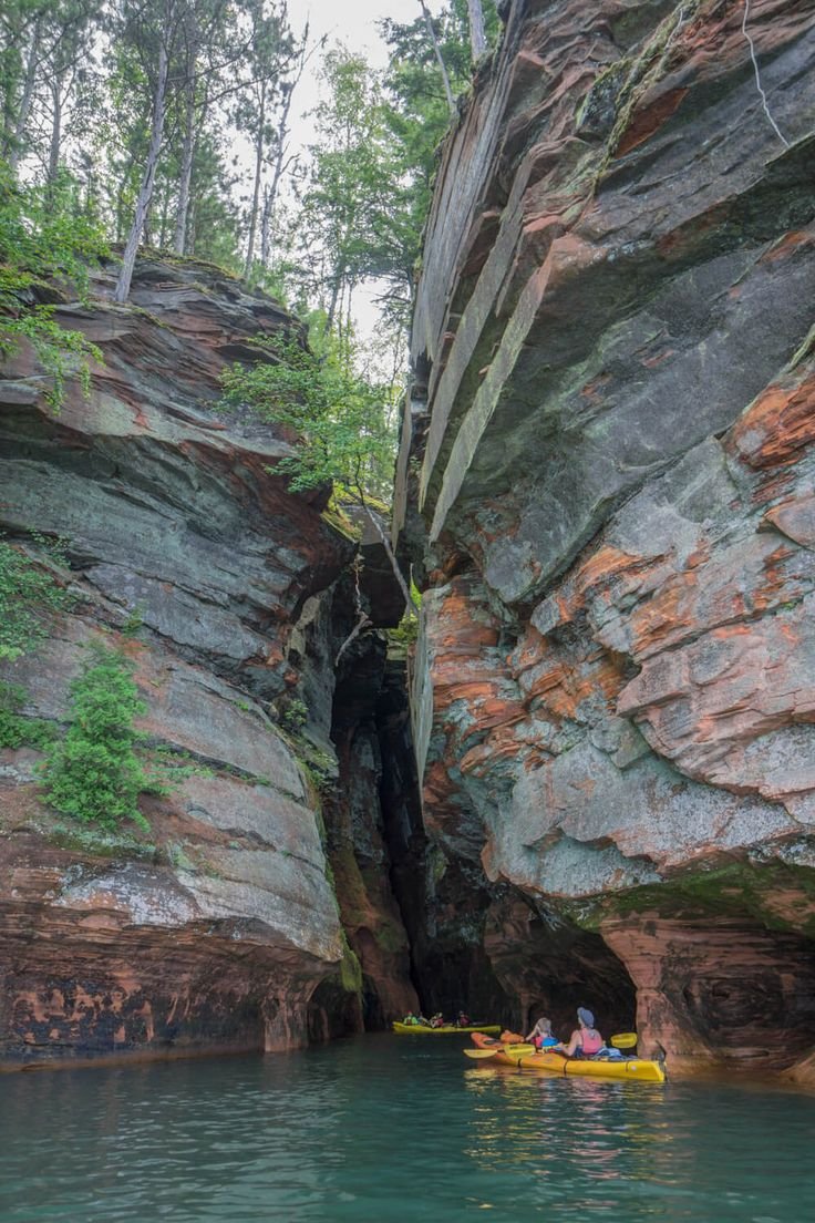 This may contain: two people are kayaking in the water near some large rocks and green vegetation on either side of them