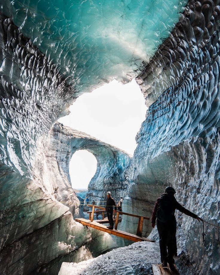 This may contain: two people are walking through an ice cave
