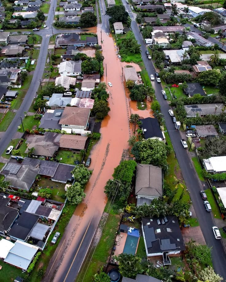 This may contain: an aerial view of a flooded street and houses in the suburbs, with water running down the road