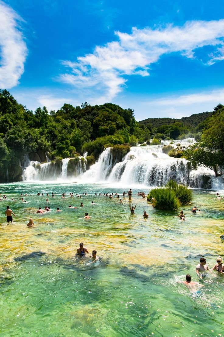 This may contain: many people are swimming in the water near a waterfall