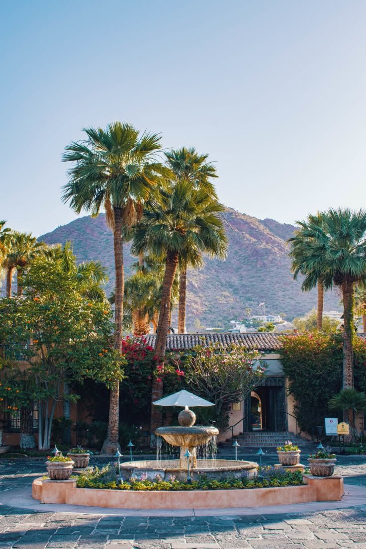 This may contain: a fountain surrounded by palm trees in front of a building with mountains in the background