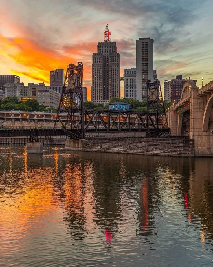 This may contain: the sun is setting over the city skyline as it reflects in the water and bridge