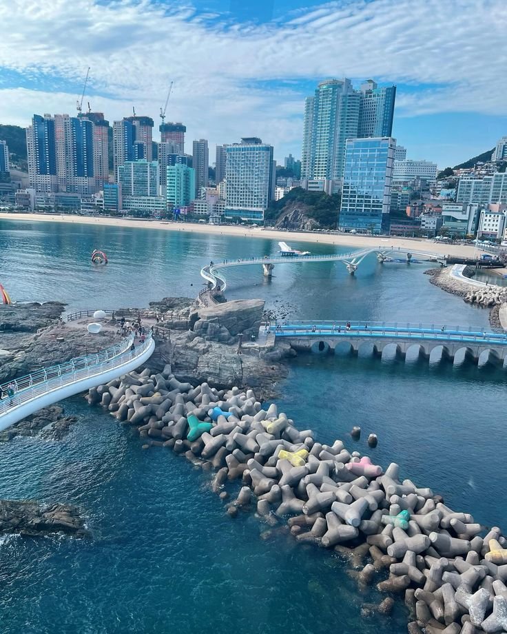 This may contain: an aerial view of a city and the ocean with people walking on rocks in the foreground