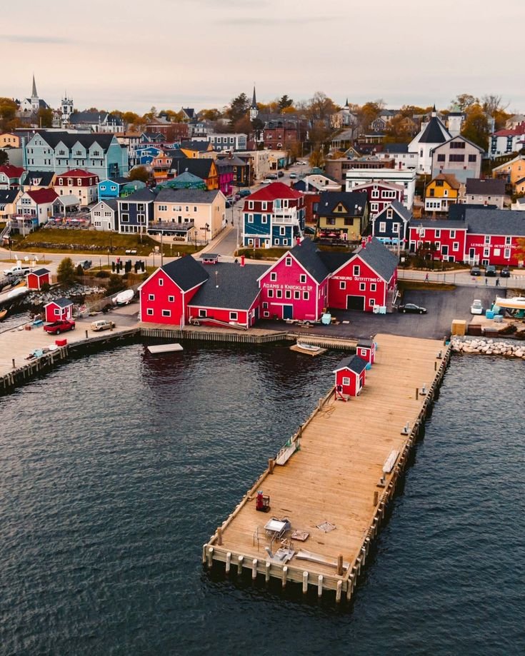 This may contain: an aerial view of a harbor with houses and boats in the water, including one red building