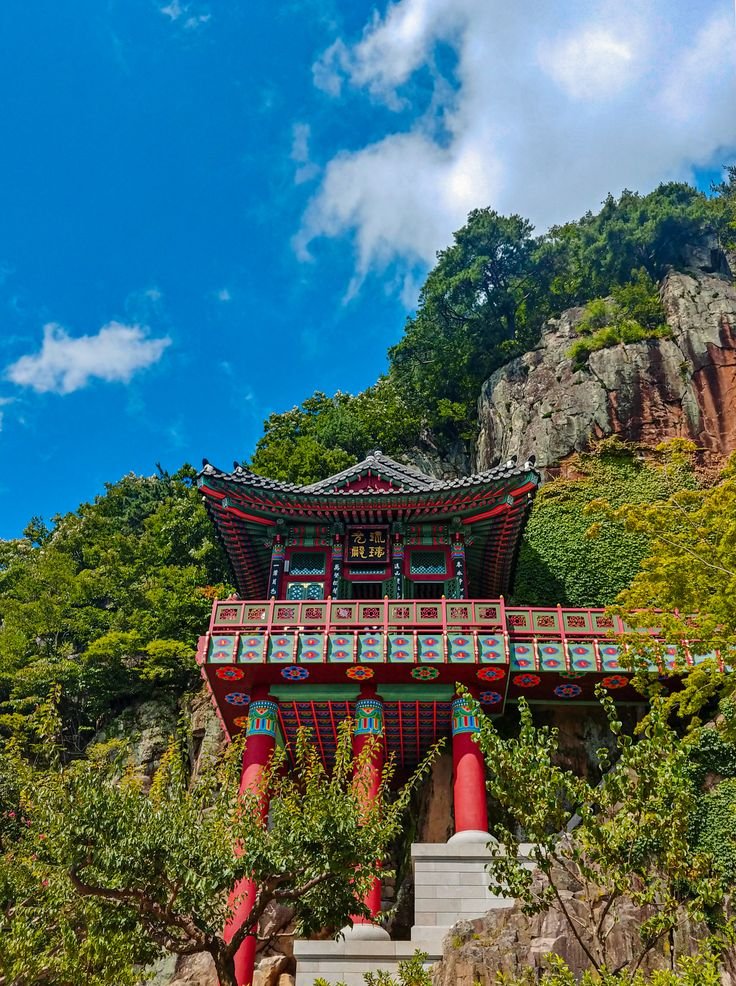 This may contain: a red and white building with a bridge over it in the middle of some trees