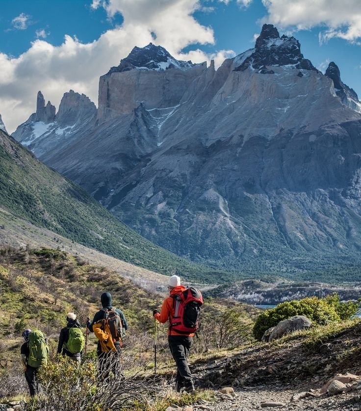 This may contain: three hikers trekking up the side of a mountain with snow capped mountains in the background