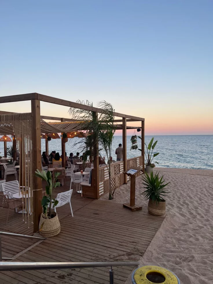 This may contain: an outdoor dining area on the beach at sunset