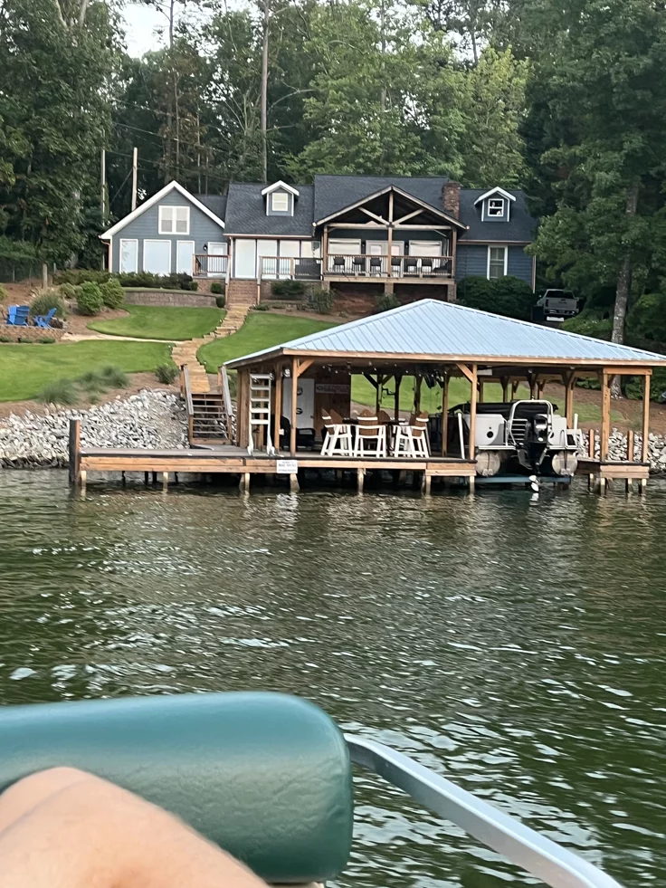This may contain: a house on the water with a boat in it's foreground and a dock at the end