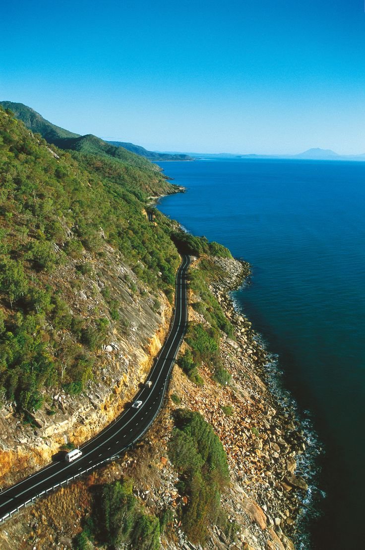 This may contain: an aerial view of a road on the side of a cliff overlooking the ocean and mountains