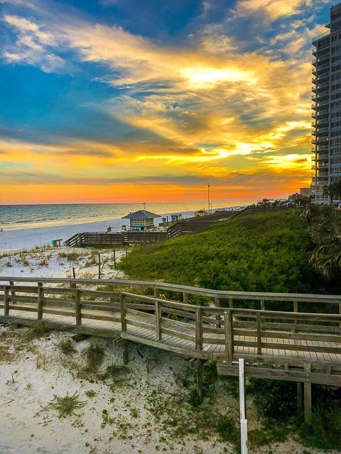 This may contain: a boardwalk leading to the beach at sunset