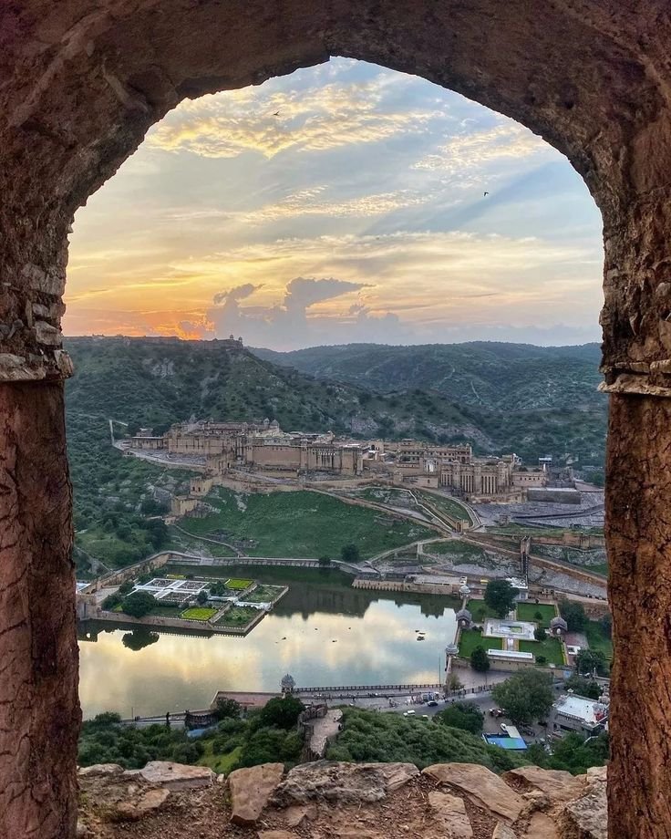 This may contain: an arch with a view of a lake and mountains in the background at sunset or sunrise