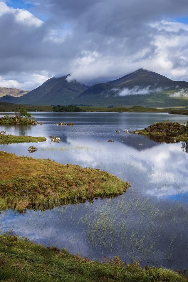 This may contain: the mountains are reflected in the still water on this cloudy day with blue sky and clouds