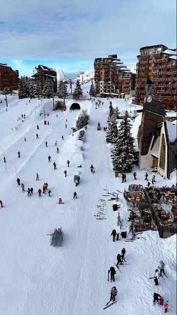 This may contain: many people are skiing down a hill in the snow near buildings and ski lifts
