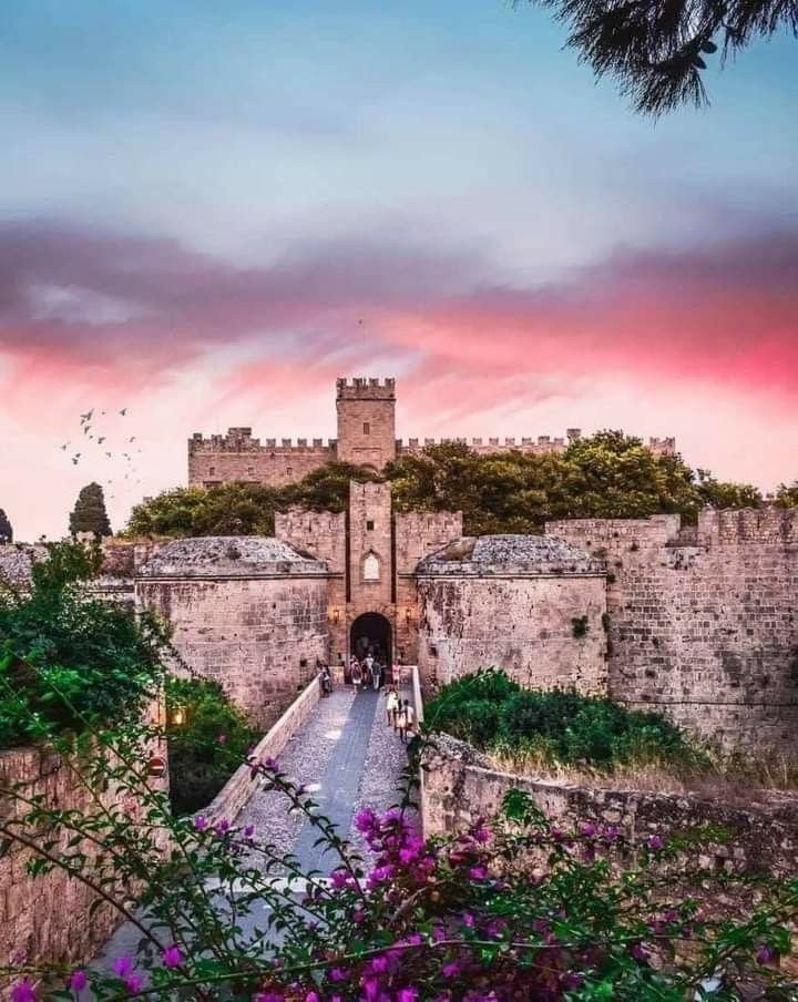 This may contain: the entrance to an old castle with flowers growing on it's sides and pink clouds in the background