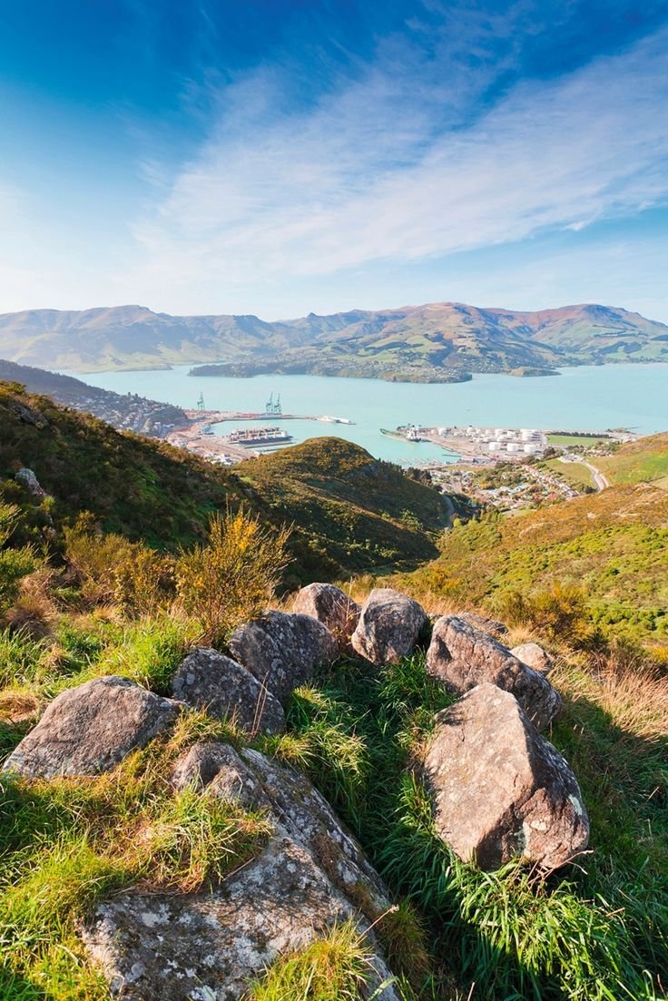 This may contain: some rocks and grass on the side of a hill with water in the back ground
