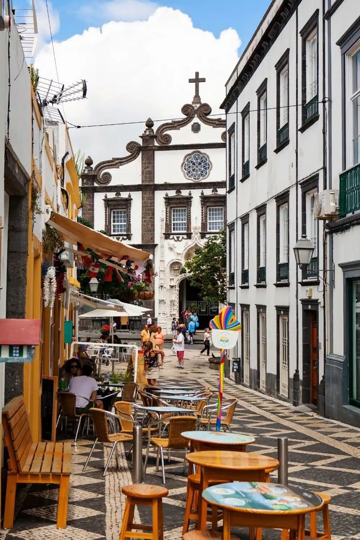 This may contain: people are sitting at tables in the middle of an alleyway with buildings on both sides