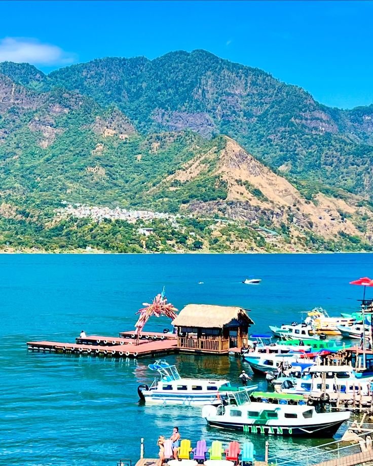 This may contain: many boats are docked at the pier in front of some mountains and blue water with people on it