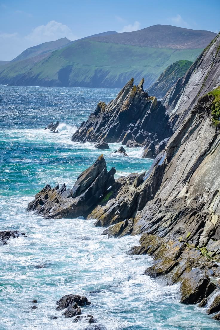This may contain: rocky coastline with blue water and mountains in the background