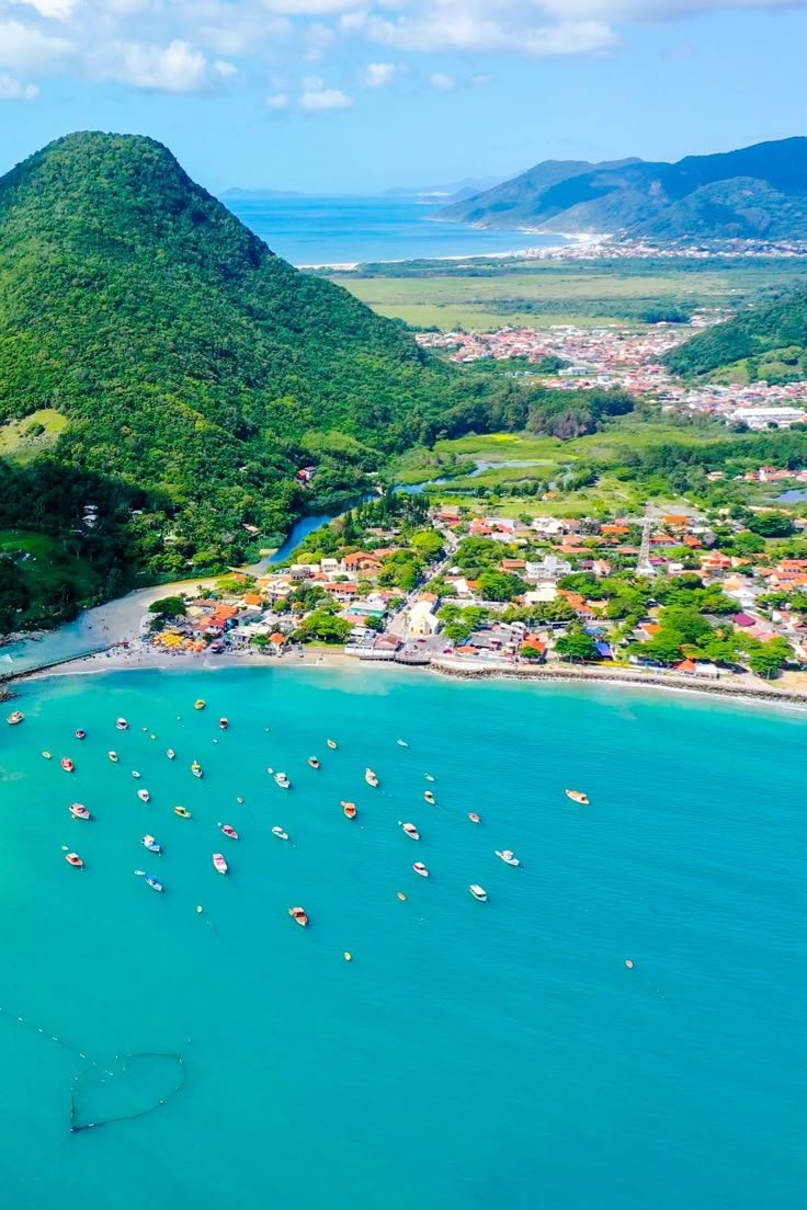 This may contain: an aerial view of boats in the water near a beach with mountains and blue sky
