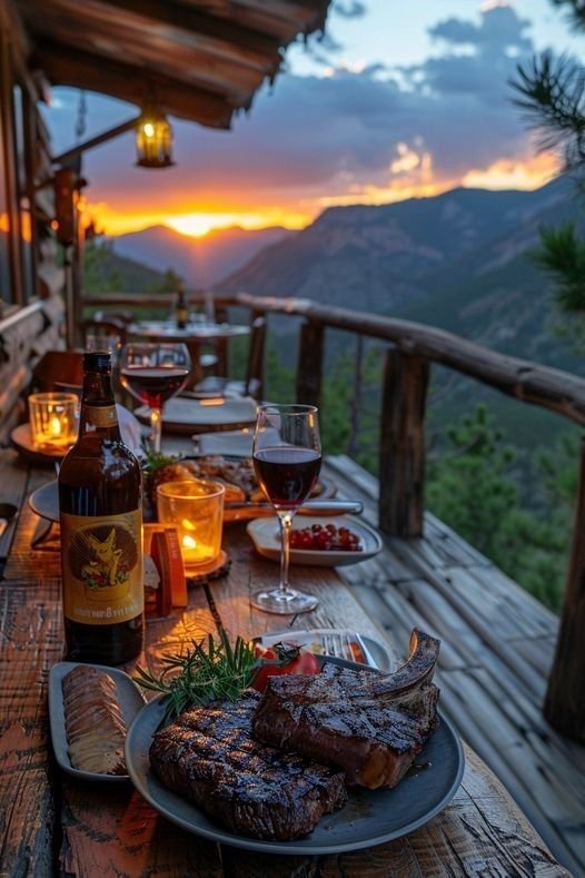 This may contain: an outdoor table with food and wine on it at dusk, overlooking the mountain range