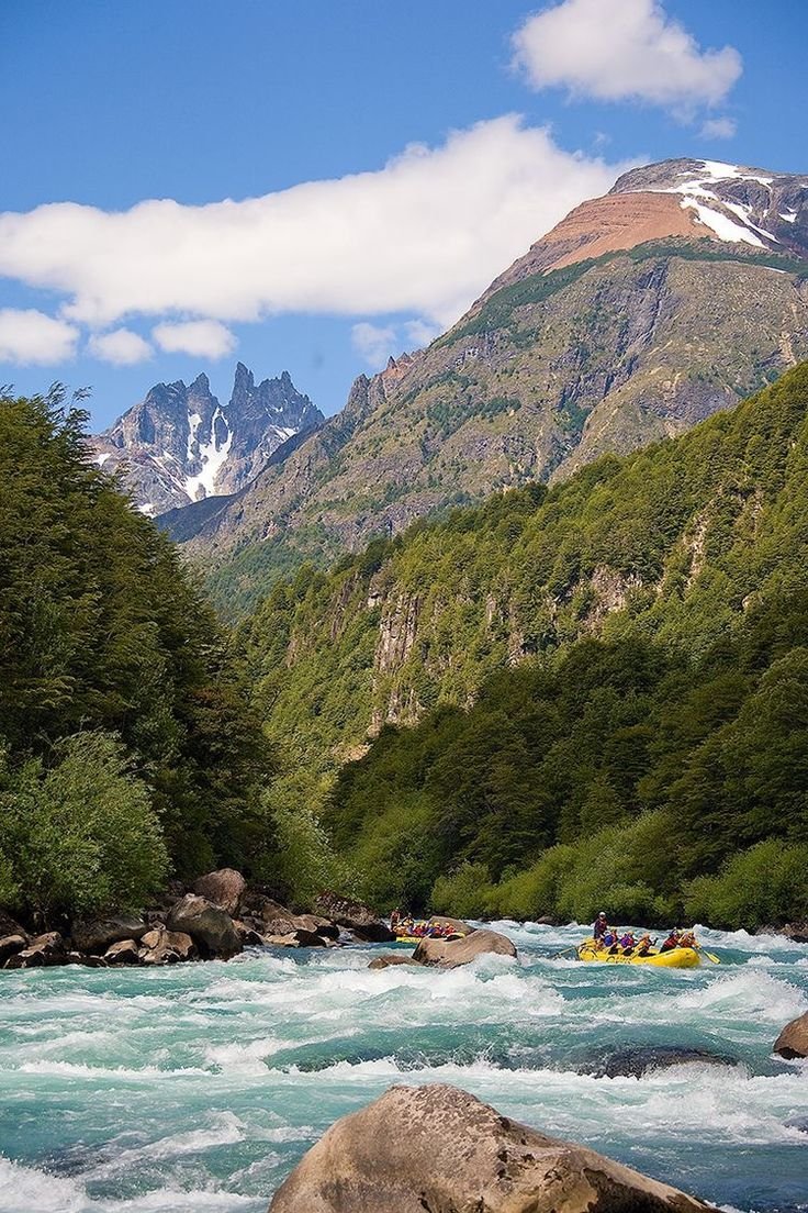This may contain: a group of people are rafting down a river in front of some mountain peaks