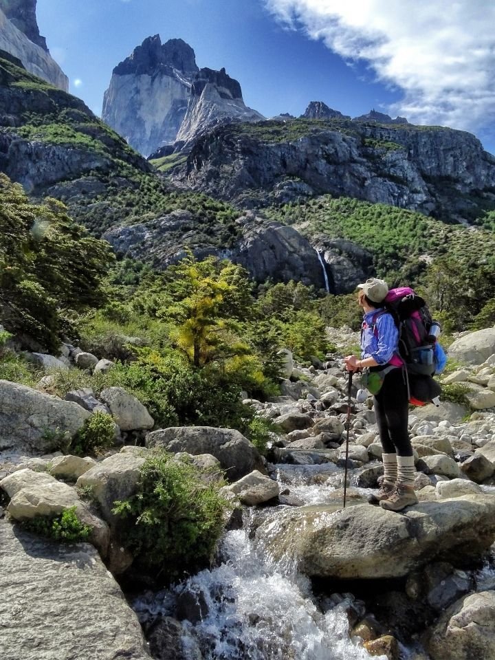 This may contain: a woman with a backpack is crossing a stream in the mountains on her hiking trip
