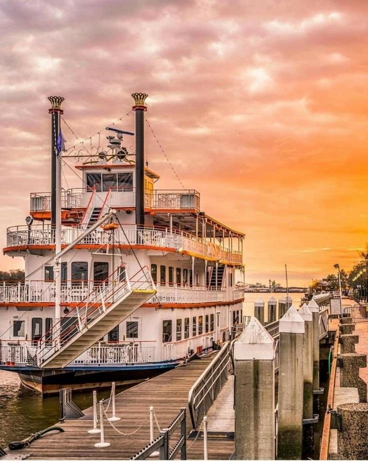This may contain: a white and blue boat docked at a pier with the sun setting in the background
