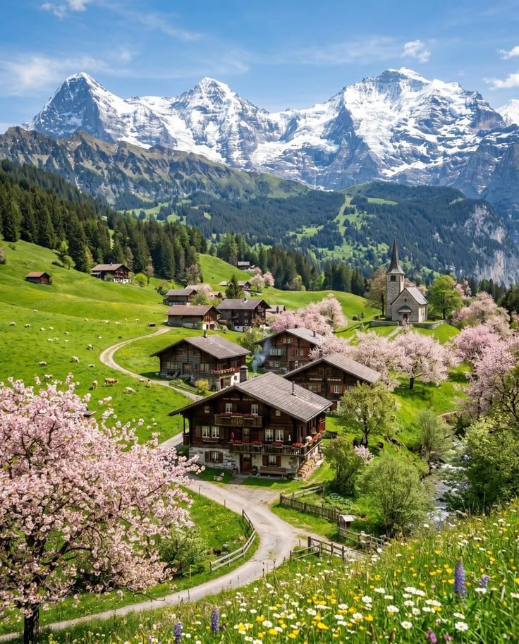This may contain: an alpine village surrounded by mountains and flowers in the foreground, with snow - capped peaks in the background
