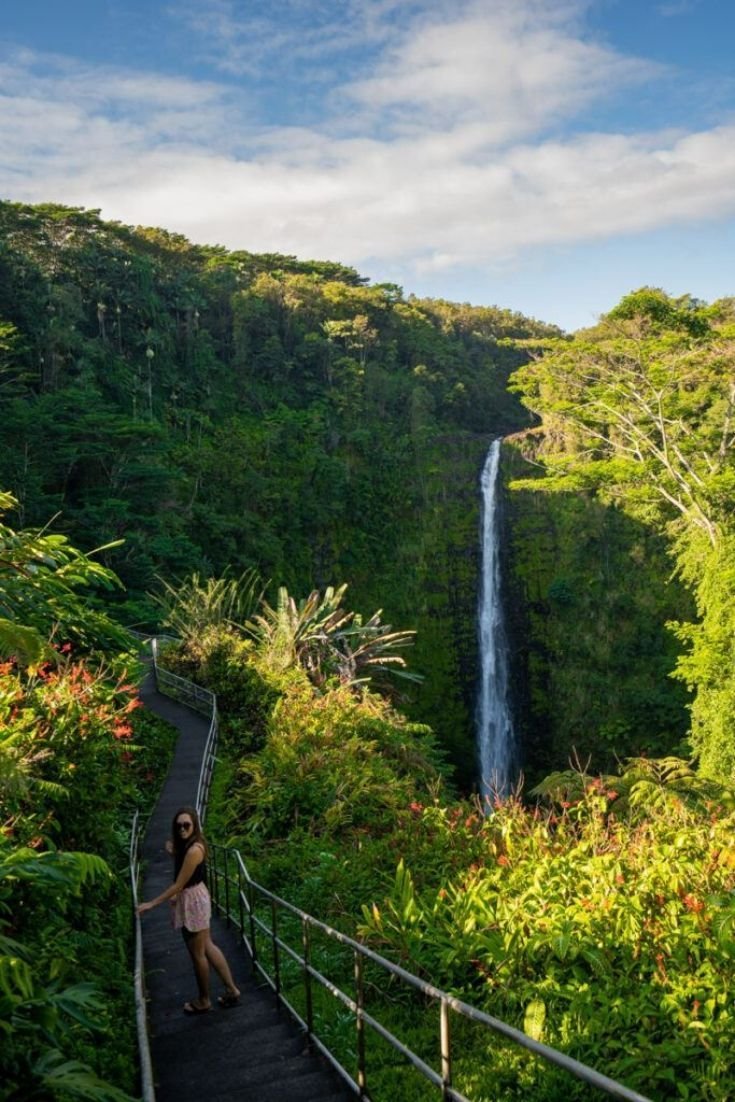 This may contain: a woman is standing at the top of a staircase near a waterfall in the jungle