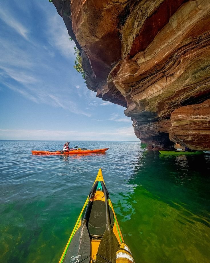 This may contain: a person in a kayak paddling through the water next to a large cliff