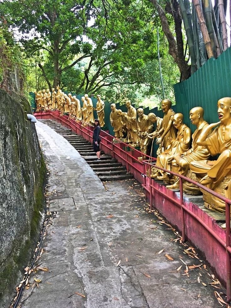 This may contain: many golden buddha statues are lined up on the steps in front of a green wall