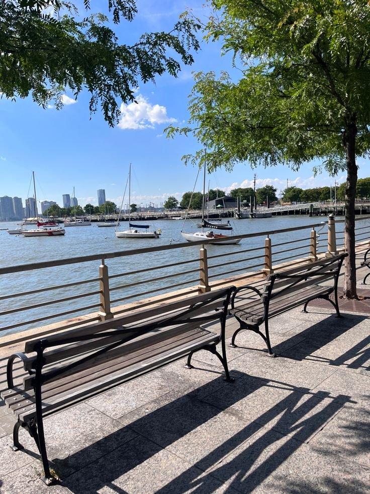 This may contain: two park benches sitting next to each other on a sidewalk near the water with boats in the background