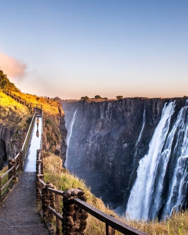 This may contain: people are walking up the side of a cliff with a waterfall in the back ground