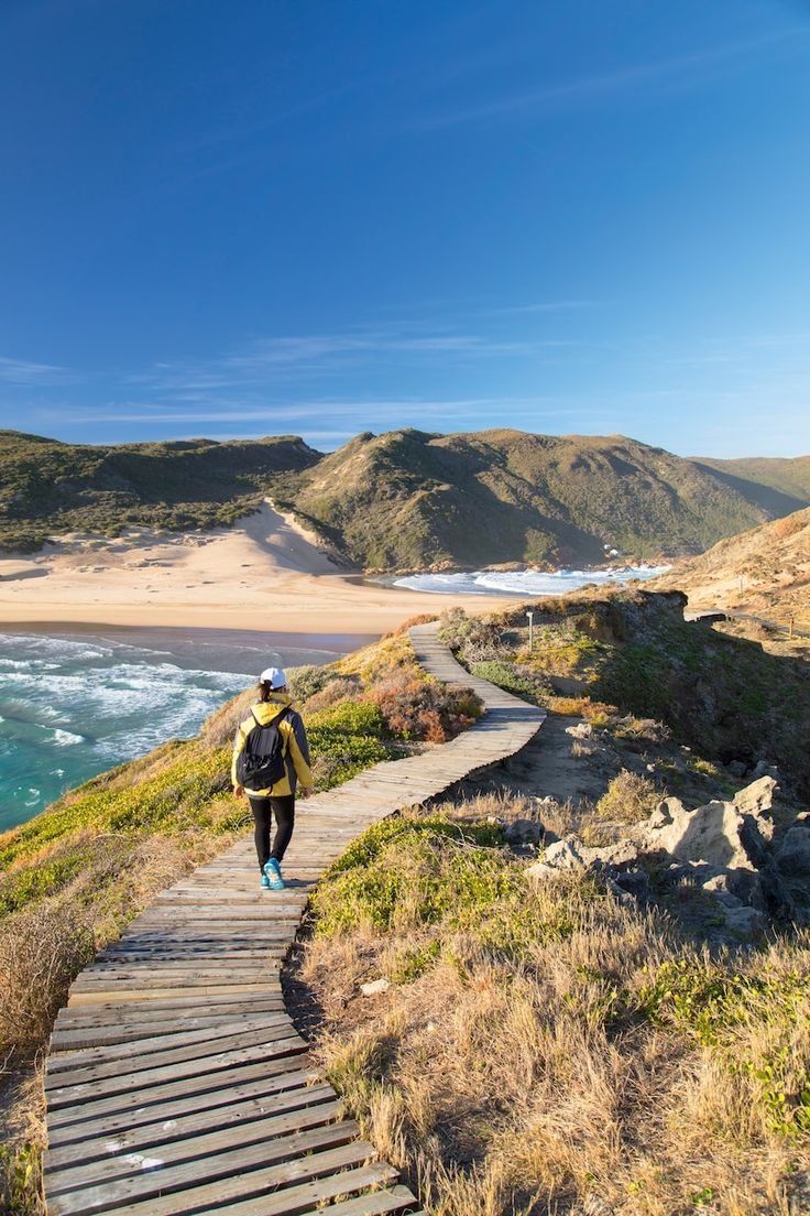This may contain: a person walking up a wooden path next to the ocean