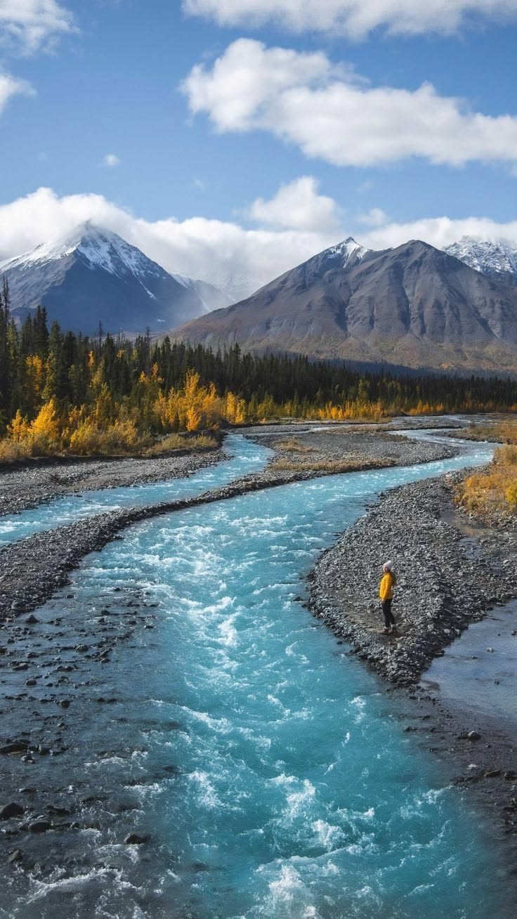 This may contain: a man standing in the middle of a river with mountains in the backgroud