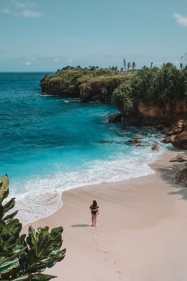 This may contain: a woman walking along the beach towards the ocean