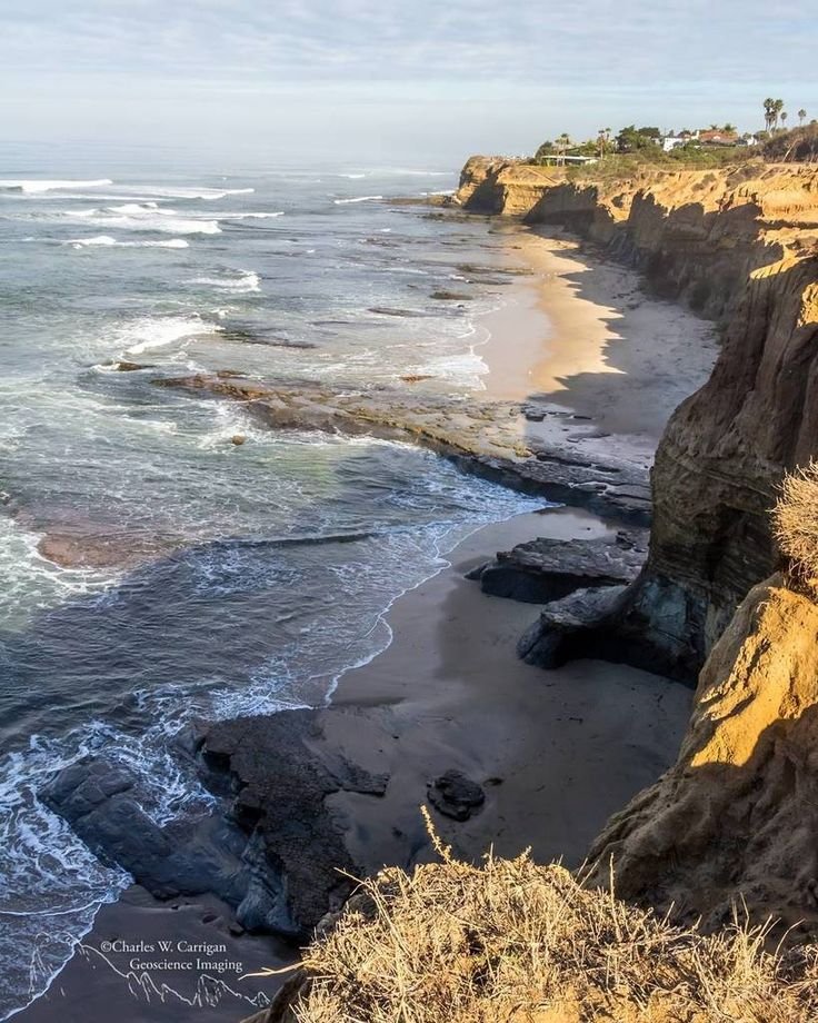 This may contain: the beach is next to some cliffs on the water's edge with waves coming in