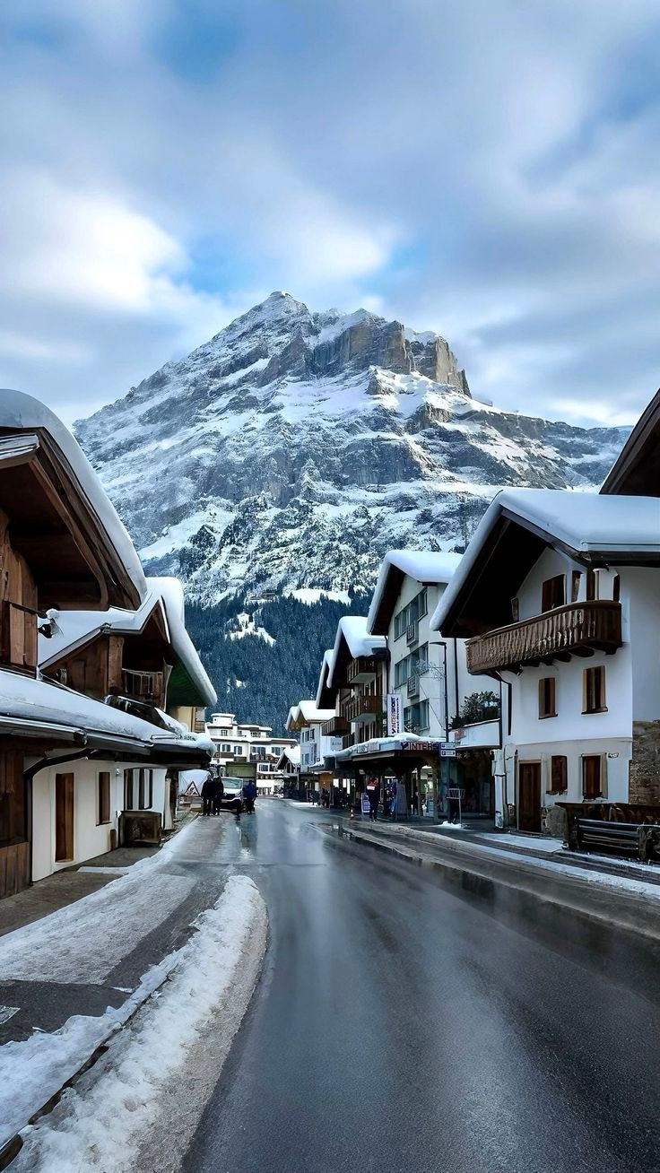 This may contain: a street with snow covered buildings and mountains in the background
