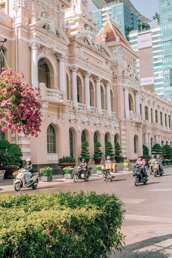 This may contain: people riding motorcycles down the street in front of a large building