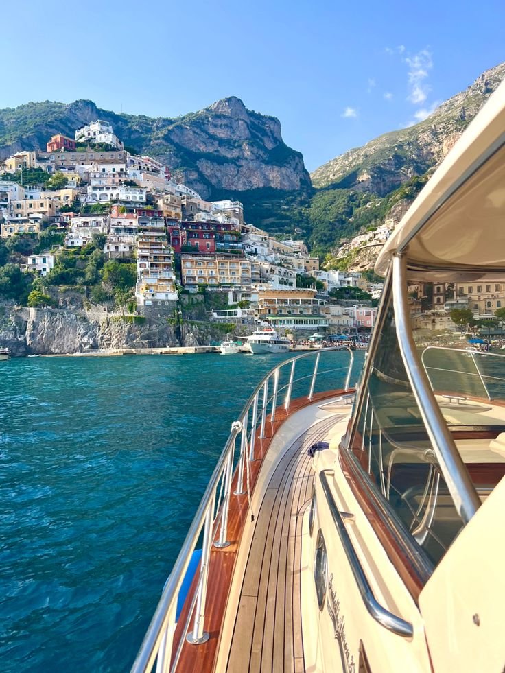 This may contain: a boat traveling on the water with houses in the background and mountains to the side