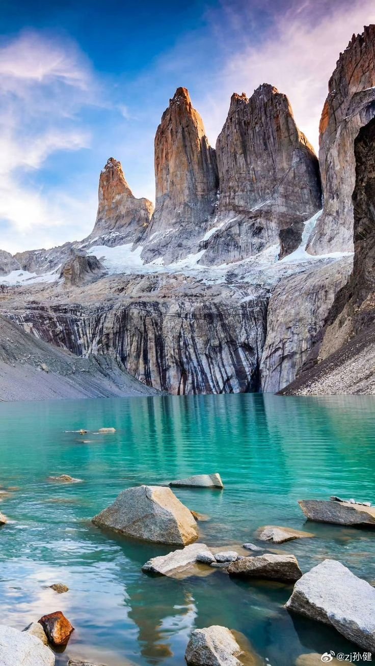 This may contain: the mountains are covered in snow and blue water, with rocks on the ground near them