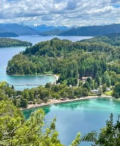 This may contain: an aerial view of a lake surrounded by trees and mountains in the distance with blue water