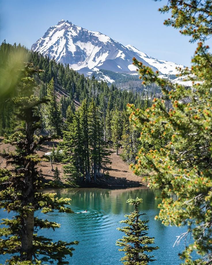 This may contain: a lake surrounded by trees and snow capped mountain in the distance with blue water below