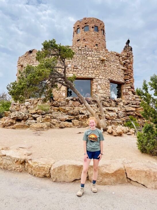 This may contain: a woman standing in front of a stone building with a tree growing out of it