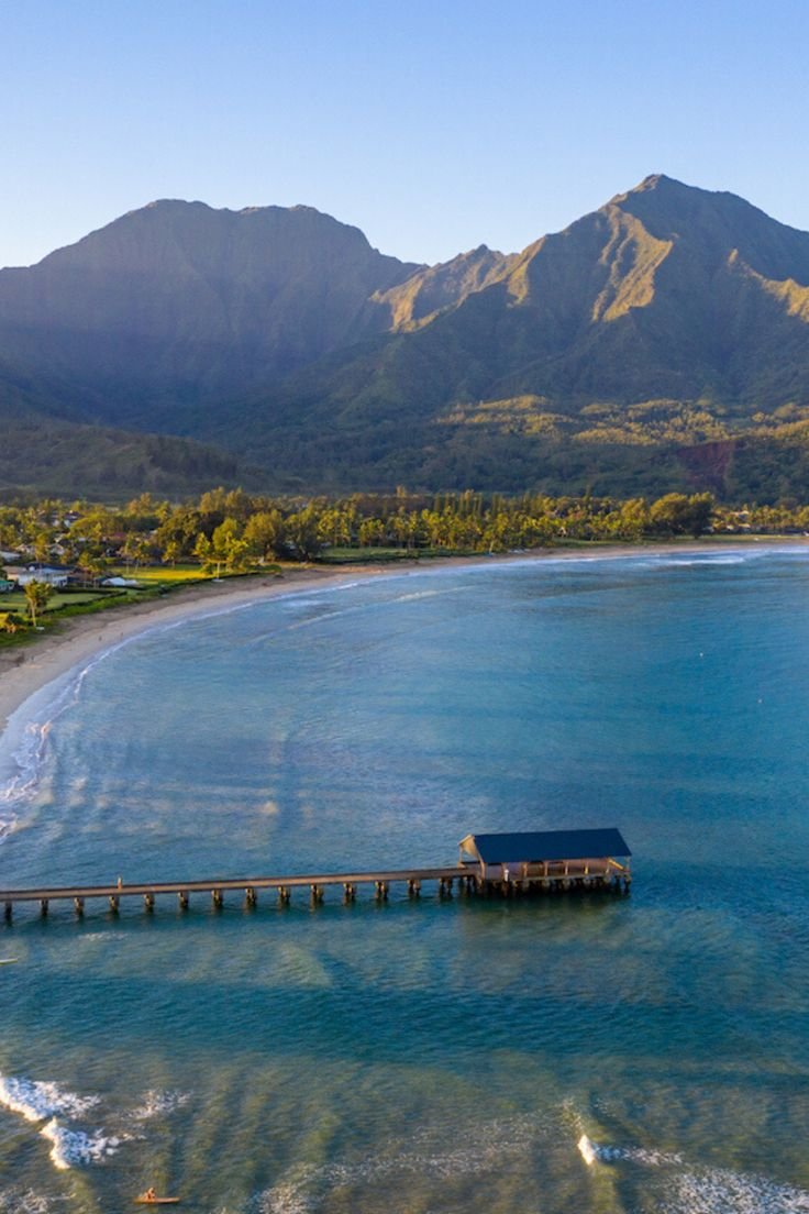 This may contain: an aerial view of the ocean with mountains in the background and a pier extending into the water