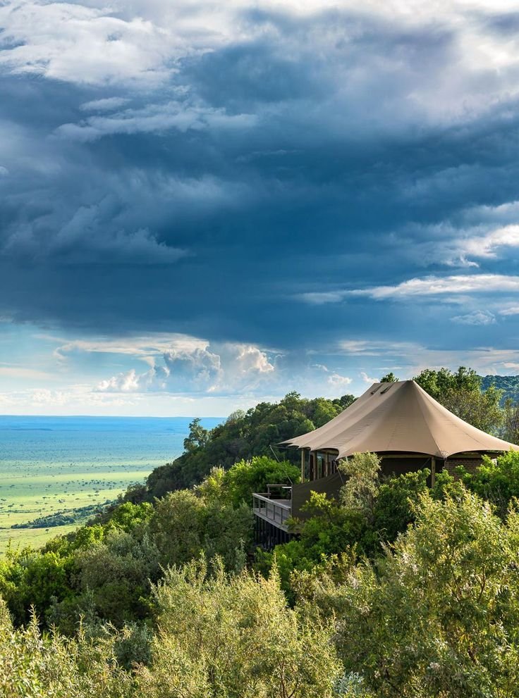 This may contain: a tent is set up on top of a hill with trees and bushes around it