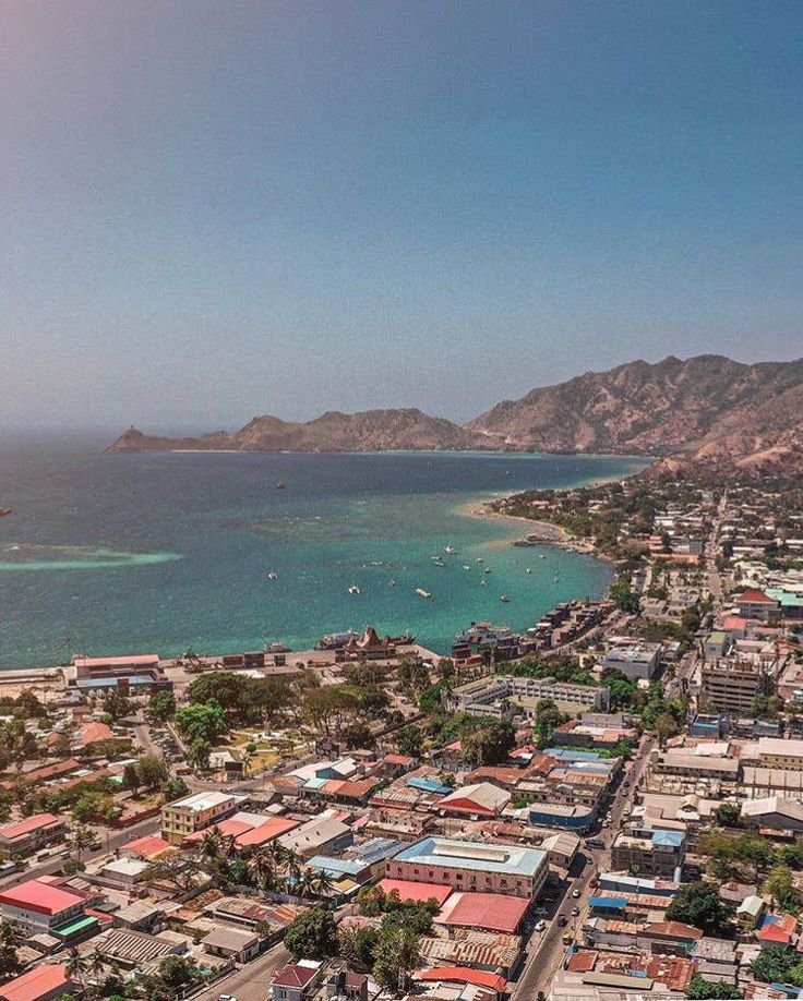 This may contain: an aerial view of a city next to the ocean with mountains in the back ground