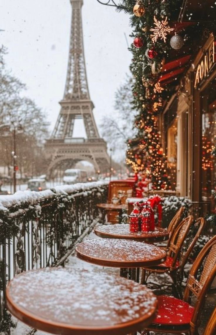 This may contain: the eiffel tower is covered in snow as seen from an outdoor cafe with tables and chairs