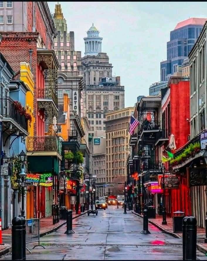 This may contain: an empty city street with buildings on both sides and people walking down the sidewalk in the distance