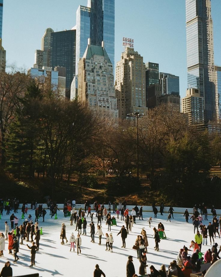 This may contain: many people are skating on an ice rink in central park, with skyscrapers in the background